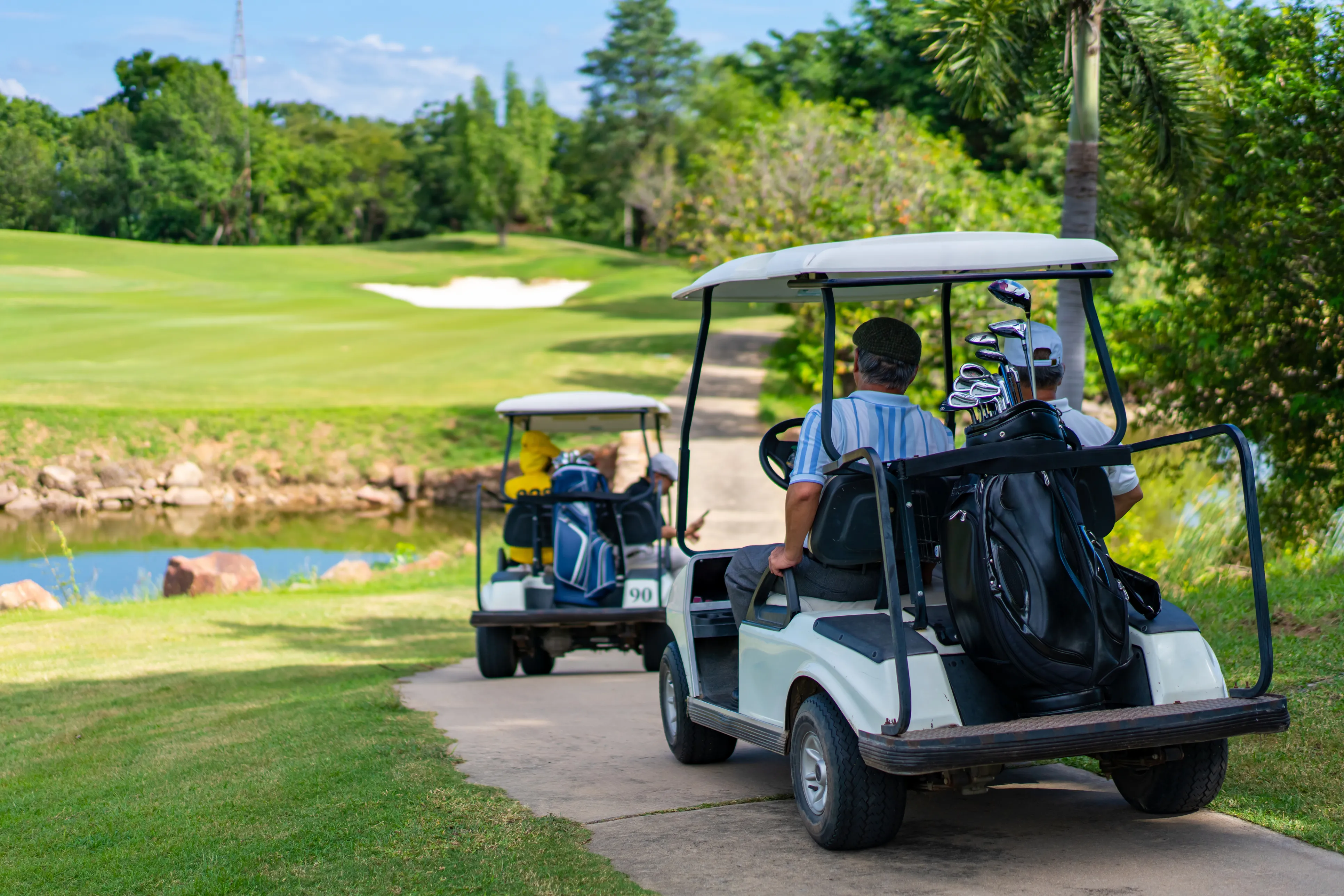 Golfers riding carts along the course beside a pond