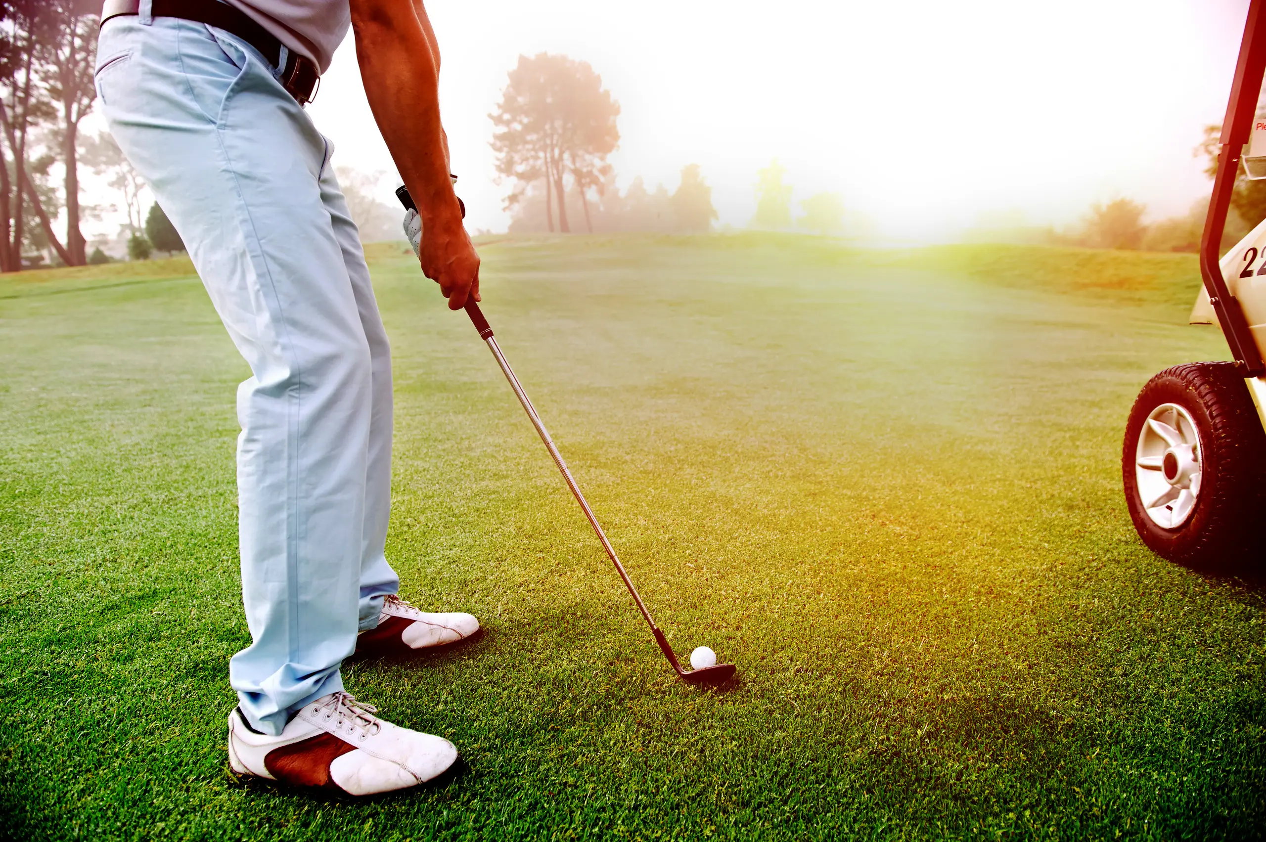 A golfer at address over the ball, early morning sun low across the fairway