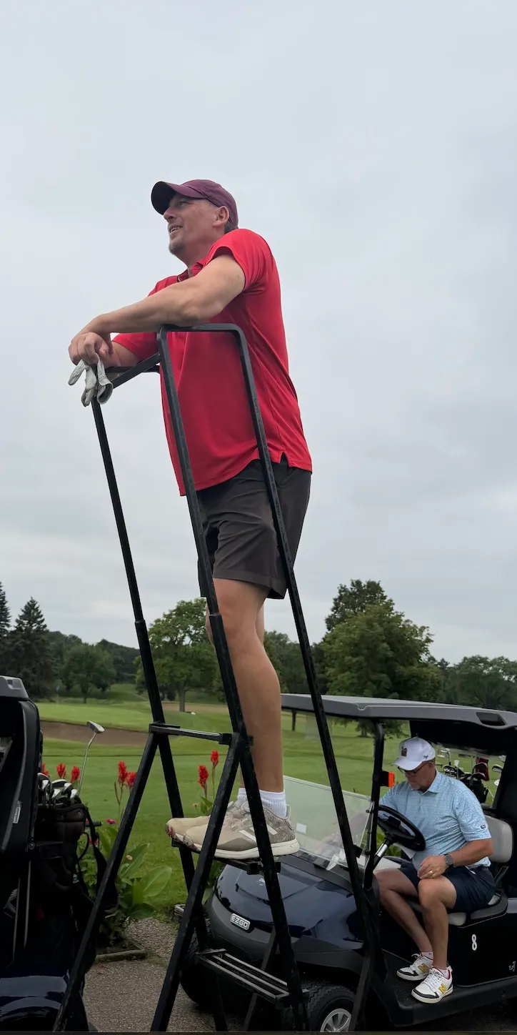 A golfer standing on a course marker, looking out over the fairway